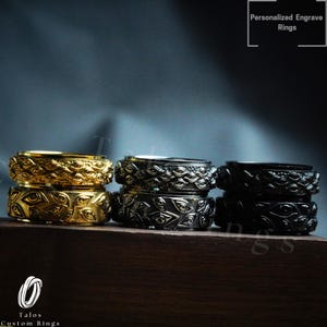 May include: A selection of stacked rings in gold, silver, and black, adorned with an eye motif. The rings are presented on a wooden surface with a dark backdrop. The text at the top says "Personalized Engrave Rings."