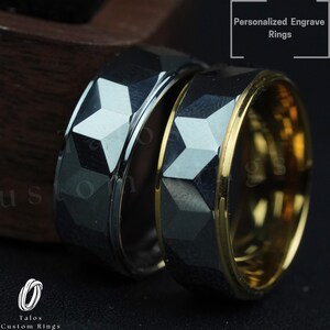 May include: Two wedding bands with a geometric design. One band is black with a gold edge, and the other is silver with a black edge. The bands are on a dark wooden surface.  Personalized Engrave Rings.