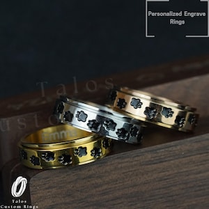 May include: Three spinning rings with paw print designs. The rings are gold, silver, and rose gold. The rings are engraved with the word "Emma".