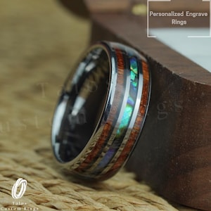 May include: A silver tungsten carbide ring with a wooden inlay and abalone shell accents. The ring has a polished finish and is engraved with the words "Personalized Engrave Rings".