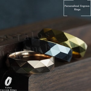 May include: Three men's wedding bands with a geometric design. The bands are made of gold, black, and silver. The bands are on a wooden surface. Personalized Engrave Rings.