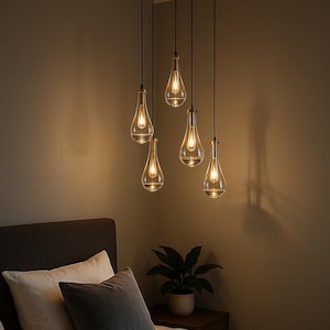 Puede incluir: Un moderno candelabro con seis luces colgantes de vidrio en forma de lágrima. Cada luz tiene un acento metálico dorado y una bombilla cálida y brillante. La lámpara cuelga de una placa de techo circular marrón oscuro, iluminando un dormitorio.