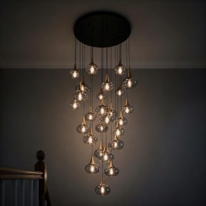 May include: A modern chandelier with multiple teardrop-shaped glass light fixtures. Each light has a gold-colored base and hangs from a black ceiling plate. The lights are illuminated, casting a warm glow.