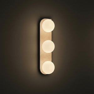 May include: A modern wall sconce with three spherical, frosted glass light bulbs. The bulbs are arranged vertically on a rectangular, beige-colored backing. The sconce is mounted on a dark brown wall, creating a contrast.