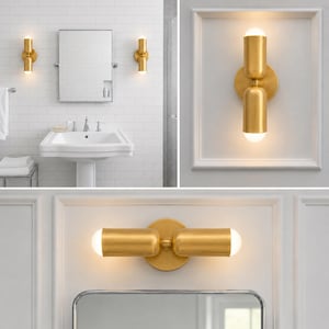 May include: Gold-coloured bathroom wall lights with a cylindrical design. The lights are mounted on a white wall and emit a warm glow. The bathroom features a white sink, mirror, and tiled walls, creating a modern aesthetic.
