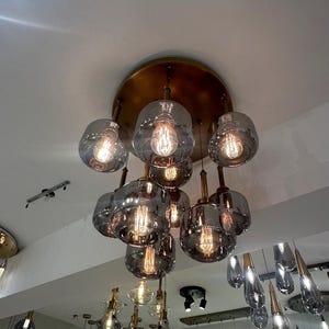 May include: A white ceramic mug with a black handle and the text "But First, Coffee" in a bold, black font. The mug is set against a blurred background, suggesting a cozy setting.