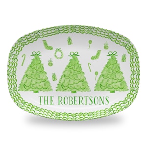 May include: White oval serving platter with a green border featuring a repeating wave pattern. The center of the platter has three green Christmas trees with green ornaments, candy canes, and gift boxes. The text "THE ROBERTSONS" is printed in green below the trees.