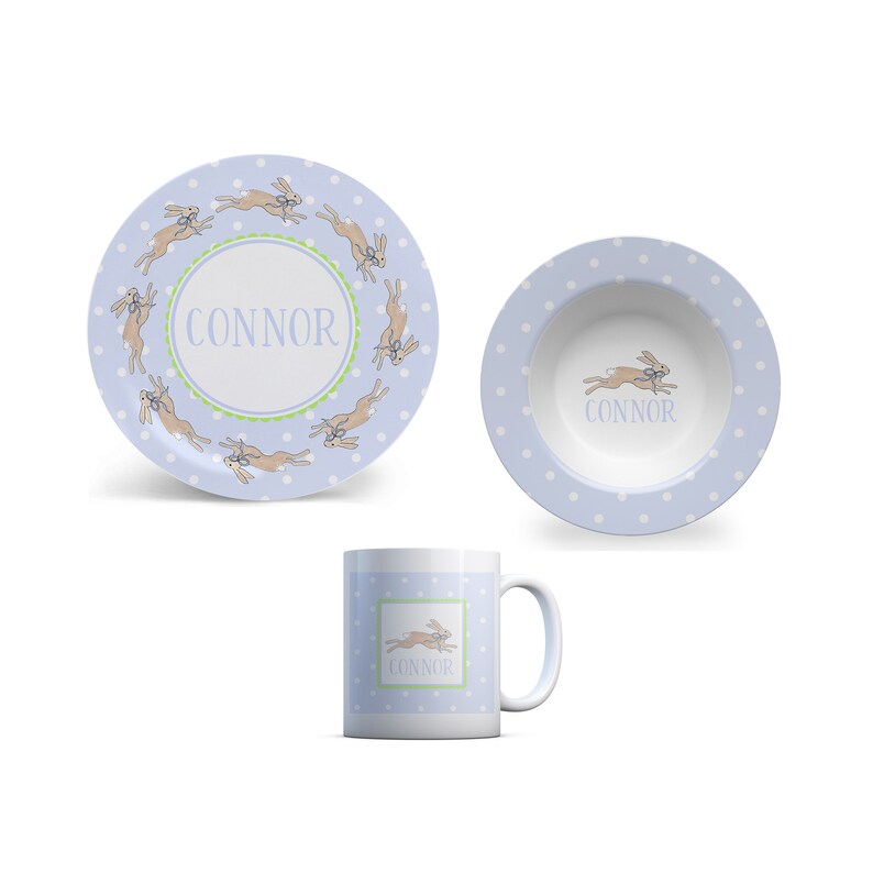 May include: A blue and white personalized children's dinnerware set with a bunny rabbit design. The set includes a plate, bowl, and mug. The name "CONNOR" is printed on each piece.