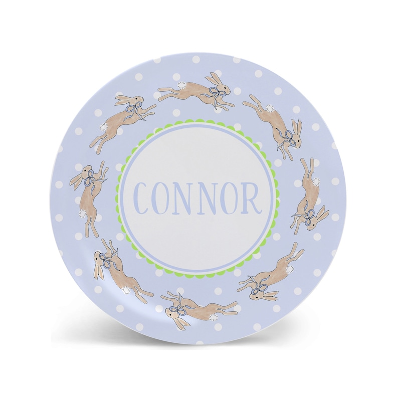 May include: A blue and white personalized plate with a green border and a circle in the center that says "CONNOR". The plate is decorated with a pattern of white dots and brown bunnies with blue bows.