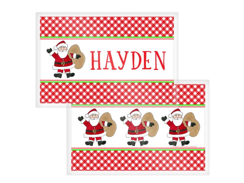 May include: Christmas-themed rectangular placemats with a red and white checkered pattern. Each placemat features a Santa Claus illustration carrying a sack. The name "HAYDEN" is printed in red on one of the placemats.