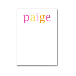 May include: A white notepad featuring the name "paige" in pink, yellow, and orange letters. The notepad is rectangular and has a simple design. The letters are in a playful, colourful font.