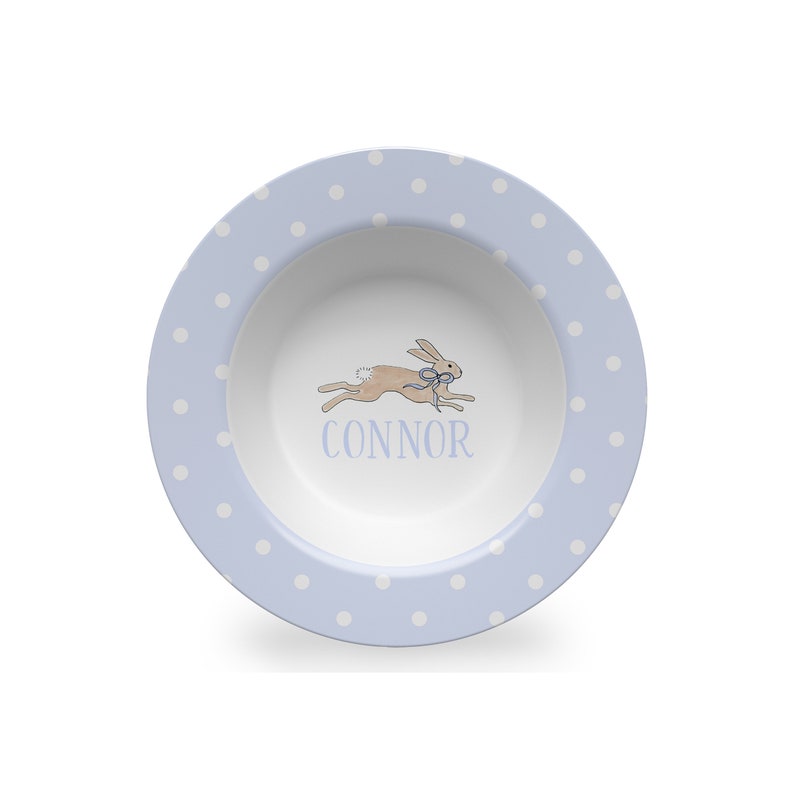 May include: A light blue ceramic bowl with white polka dots. The bowl features a running rabbit illustration and the name "CONNOR" in blue lettering.