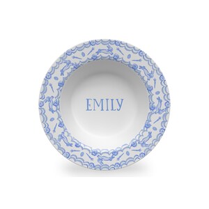 Puede incluir: Un taz&oacute;n de cer&aacute;mica blanco con un patr&oacute;n de conejo azul y blanco alrededor del borde. El taz&oacute;n tiene el nombre "EMILY" escrito en azul en el centro.