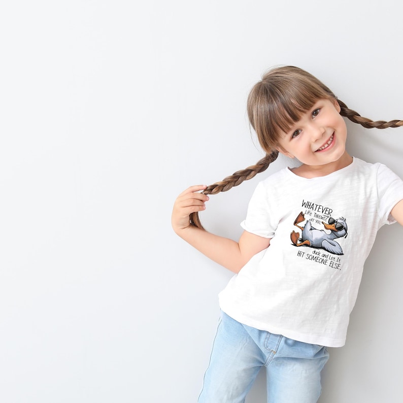 May include: White t-shirt featuring a cartoon duck wearing sunglasses and the text "WHATEVER Life Throws at You, Duck and Let It Hit Someone Else." The duck is lying down with its feet up. The shirt is worn by a young person.