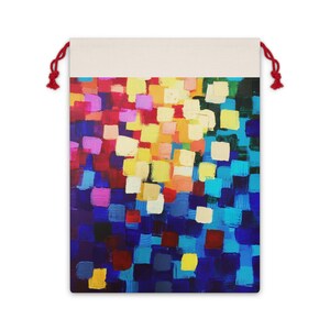 May include: A drawstring bag with a colorful abstract painting design. The artwork features a mosaic of square brushstrokes in shades of blue, red, yellow, and purple. The top of the bag is a natural canvas color, and it has red drawstrings.