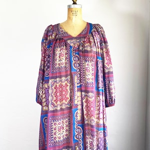 May include: A vintage dress with a patchwork design in shades of purple, blue, and gold. The dress features a V-neck, long sleeves, and a loose, flowing silhouette. The fabric has a repeating pattern of floral and geometric shapes.
