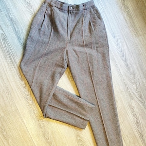 May include: A pair of brown and red plaid high-waisted trousers. The pants have a button closure, pleats at the waist, and a straight leg design. The fabric has a subtle pattern and a classic, tailored look.