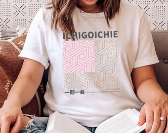 May include: White t-shirt featuring a geometric pattern in pink and gold. The text "ICHIGOICHIE" is printed in black above the pattern. Below the pattern, the text "一期一会" is printed in black, followed by the text "Every moment is a once-in-a-lifetime opportunity."