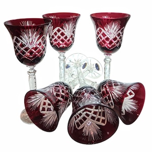 May include: A collection of six ruby red crystal wine glasses. Each glass has a cut crystal design with a diamond and fan pattern. The stems are clear, and the bowls are a deep red colour.