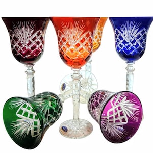 Könnte beinhalten: Eine Sammlung von sechs farbigen Kristall-Weingläsern. Die Gläser weisen aufwendige Schliffmuster auf und sind in den Farbtönen Rot, Orange, Gelb, Blau, Grün und Lila gehalten. Die Stiele sind klar, und die Gläser sind auf weißem Hintergrund angeordnet.