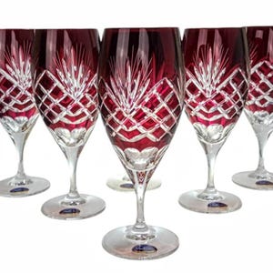 Puede incluir: Cinco copas de vino de cristal rojo rubí con intrincados patrones de corte de diamantes y hojas. Las copas tienen tallos transparentes y bases redondas. Las copas están dispuestas en fila, mostrando su elegante diseño.