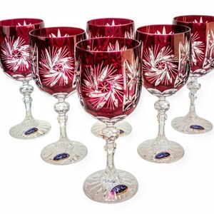 Può includere: Sei calici da vino in cristallo rosso rubino con intricati disegni incisi. I calici hanno steli e basi trasparenti e sono disposti a semicerchio. I motivi incisi sono bianchi e creano un effetto a stella. Un set classico.