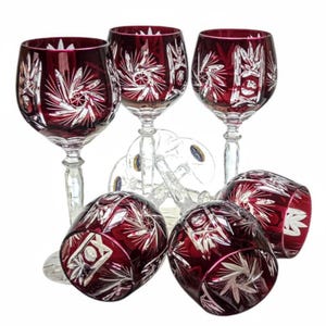 May include: Set of six red crystal wine glasses with intricate cut designs. The glasses have a clear stem and base.