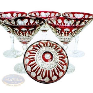 Könnte beinhalten: Set aus sechs rubinroten Kristall-Champagnergläsern mit dekorativem Muster. Die Gläser haben einen klaren Stiel und Fuß, und die Schale weist ein weißes und rotes Design auf. Die Gläser sind kreisförmig angeordnet.