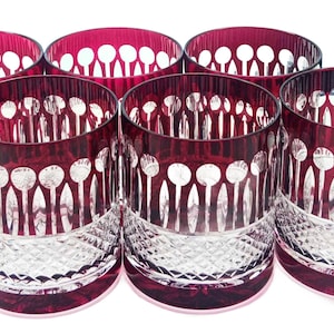May include: A set of six ruby red crystal tumblers. Each glass has a decorative cut crystal pattern and a band of ruby red around the rim. The glasses are grouped together, highlighting their elegant design.
