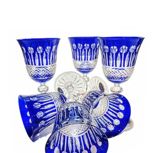 Op de afbeelding: Een verzameling kobaltblauwe kristallen wijnglazen. De glazen hebben een gedetailleerd gesneden ontwerp met een heldere kristallen voet en steel. De glazen zijn in een groep gerangschikt en tonen hun elegante vorm en ingewikkelde patronen.