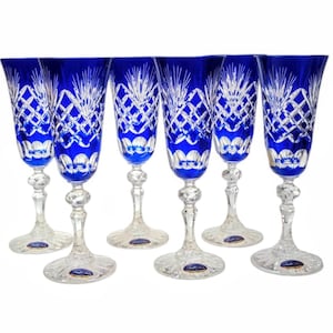 Può includere: Sei flûte da champagne in cristallo blu cobalto. Ogni flûte presenta un gambo e una base chiari e ornati, con un motivo a taglio diamante e floreale sulla coppa. I bicchieri sono disposti in fila, mostrando il loro elegante design.