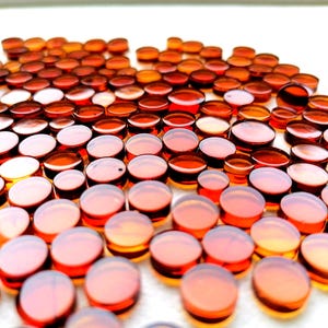 Può includere: Una collezione di piccoli tappi di vetro rotondi color ambra. I tappi sono disposti vicini, creando una superficie strutturata. Il vetro ha una qualità traslucida, con la luce che si riflette sulle superfici arrotondate.