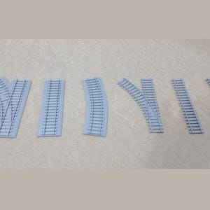 Può includere: Set di sette pezzi di binario per treni modello in plastica grigia, tra cui sezioni dritte e curve.