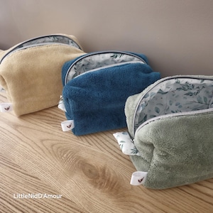 Può includere: Tre pochette con cerniera in tessuto morbido e peluche. Le pochette sono in tonalità giallo senape, blu turchese e verde salvia. Ogni pochette ha una fodera bianca con un motivo floreale. Le pochette sono disposte in fila su una superficie di legno.