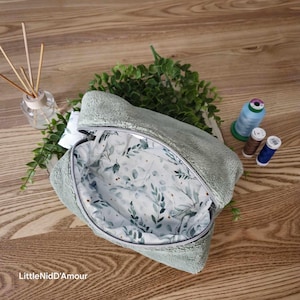 May include: A light green zippered pouch with a soft, fuzzy exterior. The pouch is open, revealing a white lining with a delicate green leaf pattern.