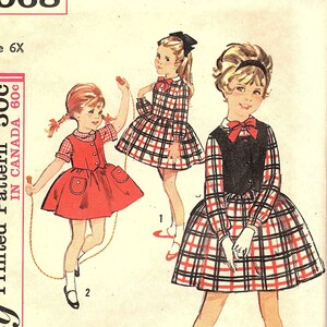May include: Simplicity sewing pattern number 5068 for a child's dress. The pattern is for size 6X and is printed in Canada. The pattern shows three girls wearing different styles of dresses. One girl is wearing a red dress with a white collar and buttons, another is wearing a plaid dress with a white collar and a black vest, and the third girl is wearing a plaid dress with a white collar and a red bow.