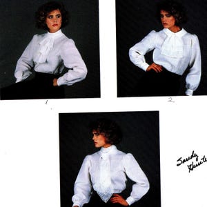 May include: A white long-sleeved blouse featuring a high collar and a ruffled jabot front. The garment has cuffed sleeves and is shown in three variations with different neck treatments, including a lace-trimmed necktie detail.