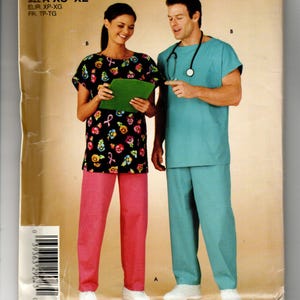 May include: A sewing pattern envelope featuring two scrub sets. One set includes a black short-sleeved top with a colorful floral and pink ribbon print paired with pink pants. The other set is a solid teal short-sleeved top and matching pants.