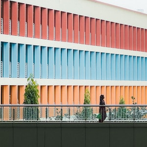 May include: A building with a colorful facade of red, blue, and orange. The building has many windows and a balcony with a railing.