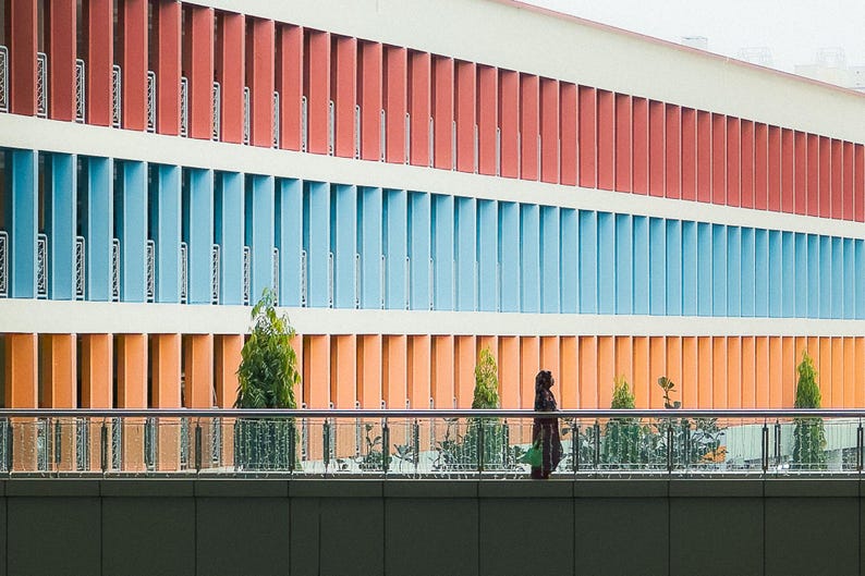 May include: A building with a colorful facade of red, blue, and orange. The building has many windows and a balcony with a railing.