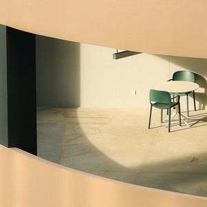 May include: A white round table with two green chairs in a modern, minimalist room with a beige wall and a black ceiling.