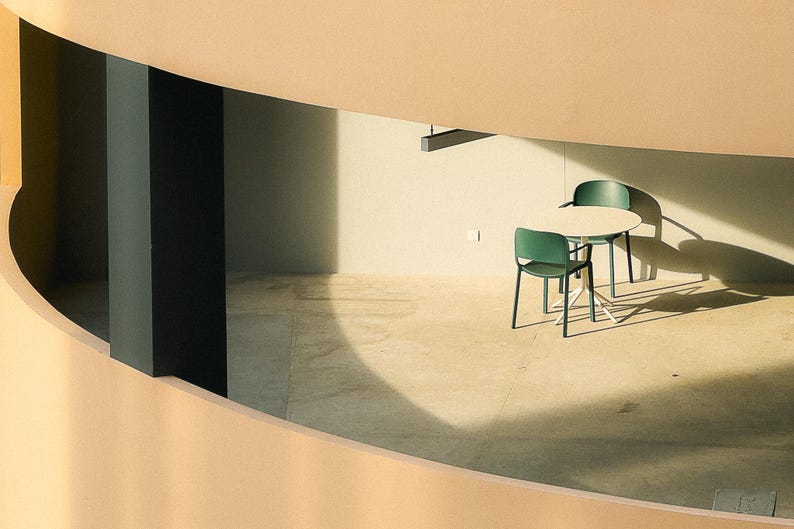 May include: A white round table with two green chairs in a modern, minimalist room with a beige wall and a black ceiling.