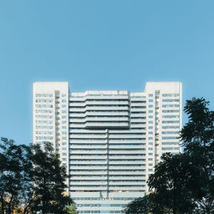 May include: A large, white, modern office building with many windows. The building is surrounded by trees.