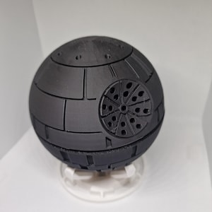 Peut inclure: Un modèle d'Étoile Noire imprimé en 3D de couleur noire avec un design détaillé et une petite base blanche.