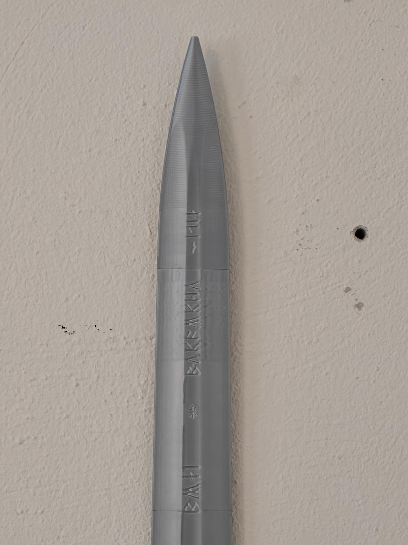 May include: A gray, bullet-shaped object with a pointed tip. The object has vertical grooves and the text "BAKEAKHA" and "BAH" printed on its side. The object is set against a neutral-colored wall.