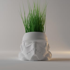 Può includere: Vaso da fiori in plastica bianca a forma di casco di Stormtrooper di Star Wars con erba verde che cresce dalla cima.