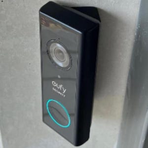 Puede incluir: Un timbre Eufy Security negro con un botón redondo de color turquesa y una lente de cámara.