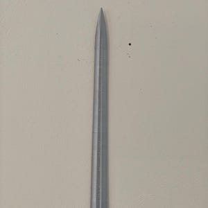 May include: A silver-colored knitting needle with a pointed tip. The needle has measurements etched along its length. The background is a neutral, off-white color.