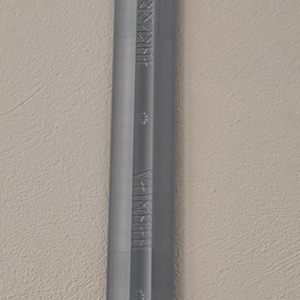 May include: A gray, elongated object with etched text and star-shaped designs. The object has a ridged texture and appears to be made of metal or a similar material. The text is in a stylized font.