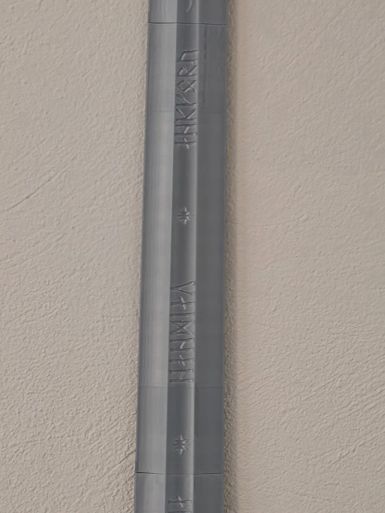 May include: A gray, elongated object with etched text and star-shaped designs. The object has a ridged texture and appears to be made of metal or a similar material. The text is in a stylized font.